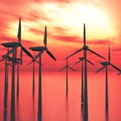 Climate Change News showing renewable energy wind turbines for combating climate change in ocean with sunset in the background.