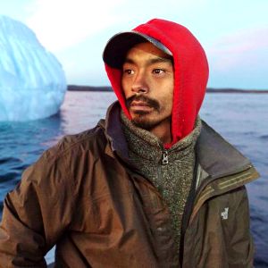 Inuit fisherman with a red hat in a boat moving around an iceberg