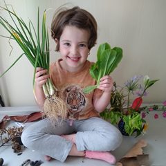 A young girl holding freshly picked green onions and romaine lettuce from a vegetable garden.
